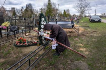 a woman weeps at the graveside of her son, where flowers cover the ground
