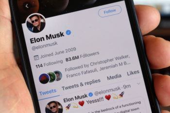 photo illustration of a person holding a phone in their hand with elon musk's twitter profile on the screen