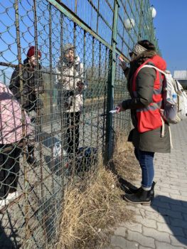a woman stands on one side of a fence speaking to three people on the other side