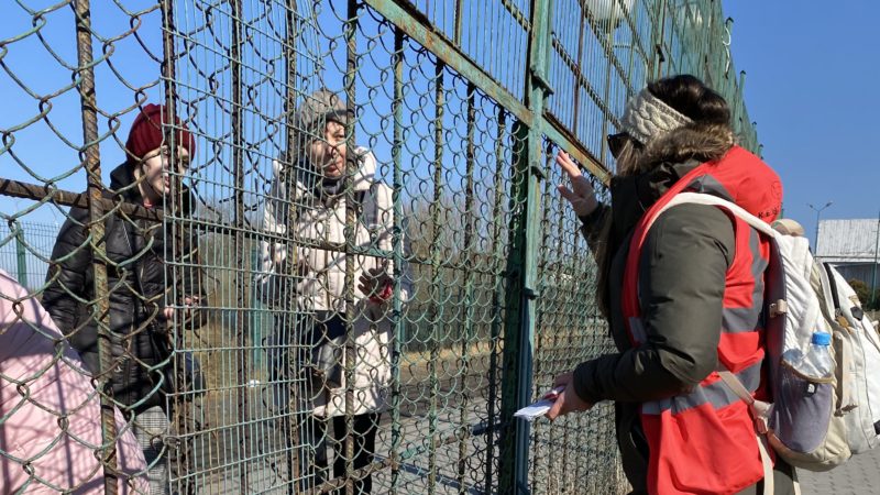 a woman stands on one side of a fence speaking to three people on the other side