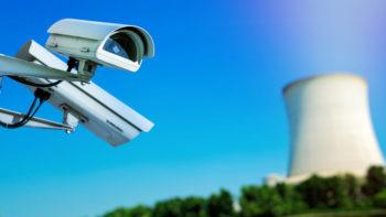 a photo showing two security cameras pointing different directions on the left and a large cooling tower in the background on the right