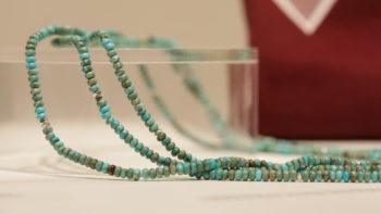 a photo of a several strands of turquoise beads on a transparent pedestal
