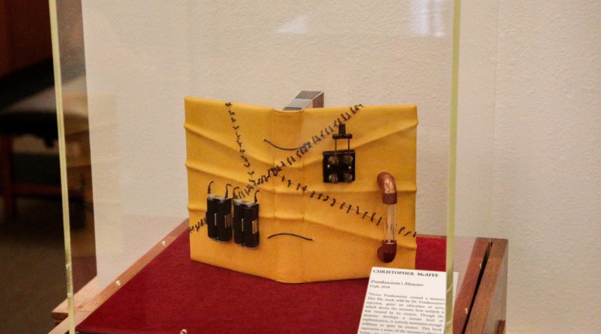 a book in a display case with a warped and stitched cover displaying wires, a switch, and a light