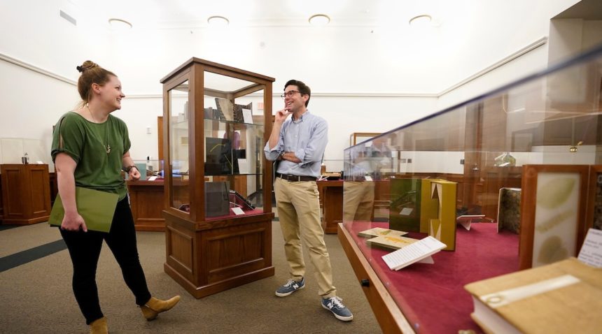 a man and a woman stand on opposite sides of a display case having a conversation