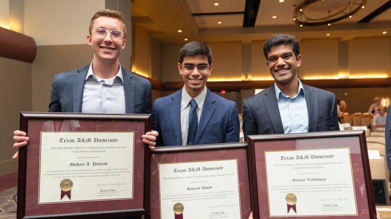 three young men in suits stand next to each other holding framed award certificates and smiling