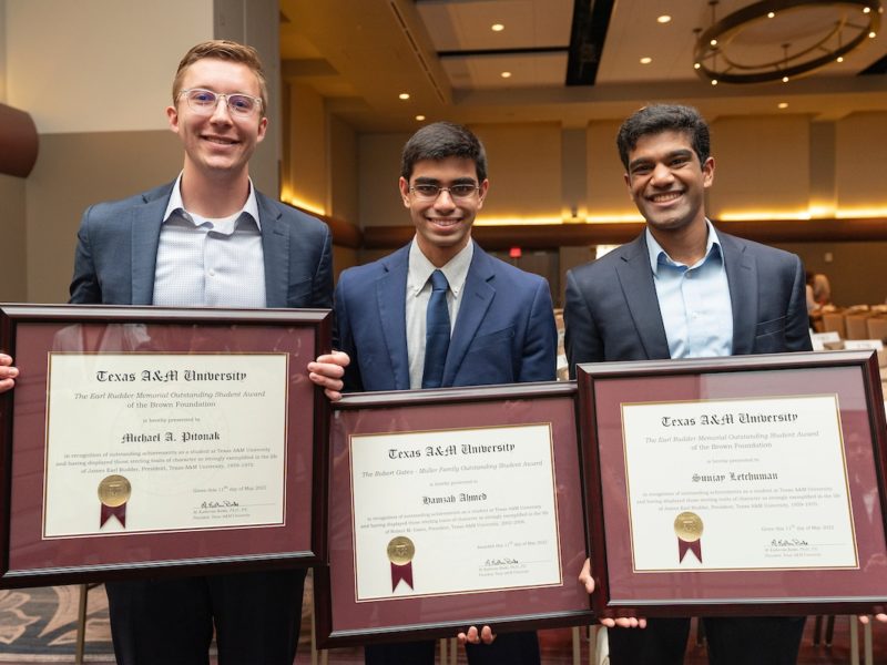three young men in suits stand next to each other holding framed award certificates and smiling