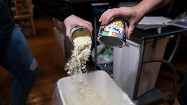 staff pour cans of powdered baby formula into a trash can
