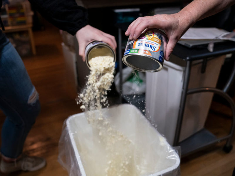 staff pour cans of powdered baby formula into a trash can