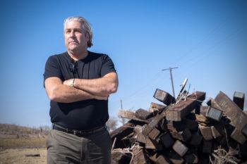 mcafee standing with his arms crossed in front of a pile of railroad ties