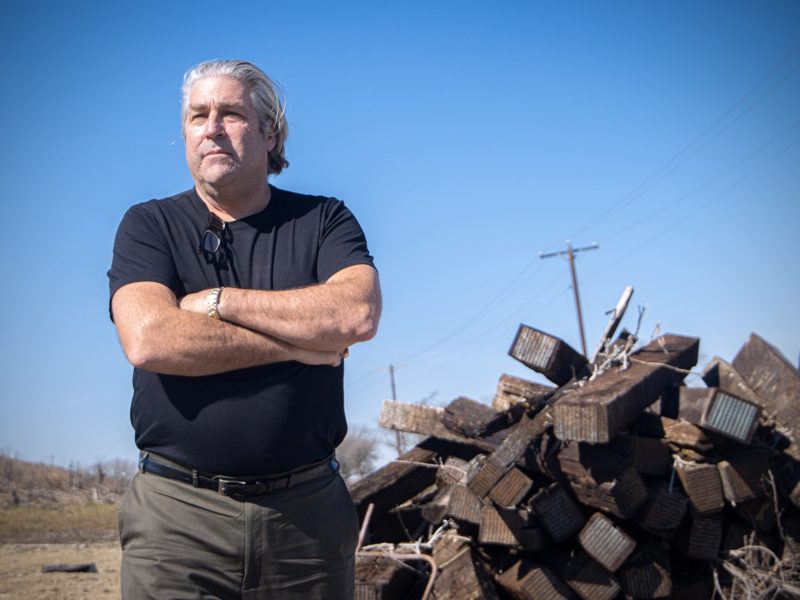 mcafee standing with his arms crossed in front of a pile of railroad ties