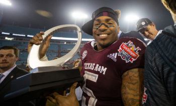 trayveon williams pictured in his a&m football uniform holding a trophy on a football field after a game