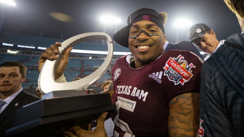trayveon williams pictured in his a&m football uniform holding a trophy on a football field after a game