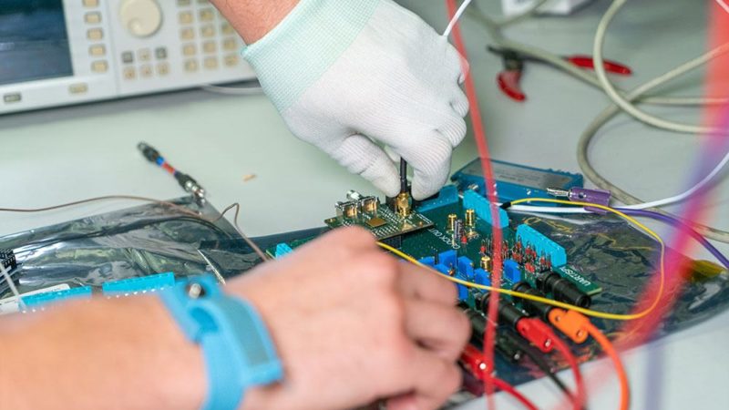 close up of person's gloved hands working on microchips with wires sticking out