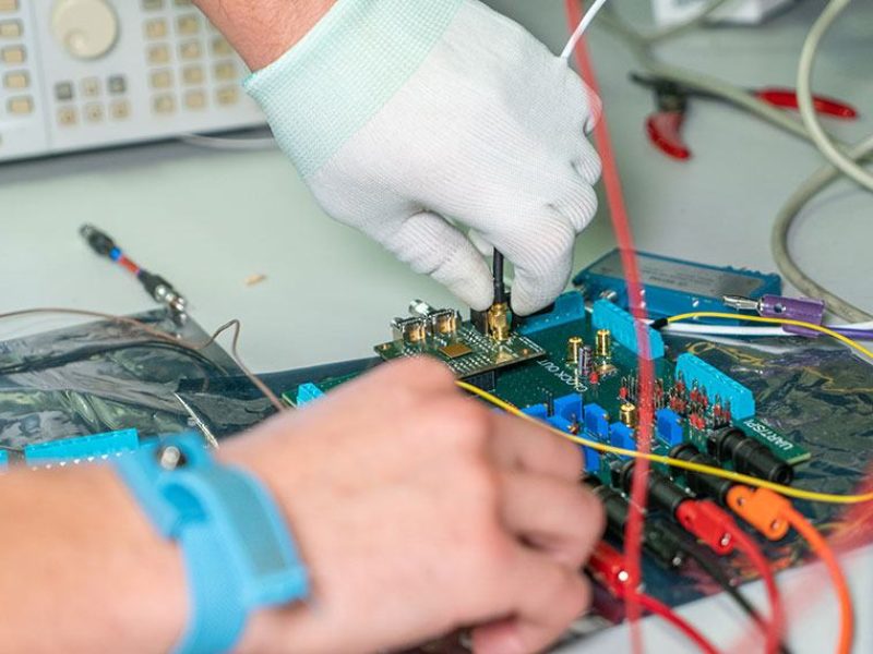 close up of person's gloved hands working on microchips with wires sticking out