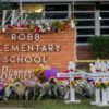 a photo of the Robb Elementary School sign in Uvalde, Texas, surrounded by flowers, crosse, candles, and other items in honor of those who lost their lives in the May 24 mass shooting