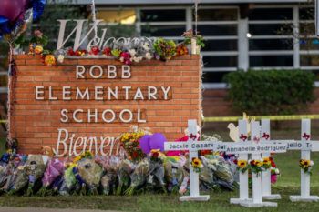 a photo of the Robb Elementary School sign in Uvalde, Texas, surrounded by flowers, crosse, candles, and other items in honor of those who lost their lives in the May 24 mass shooting