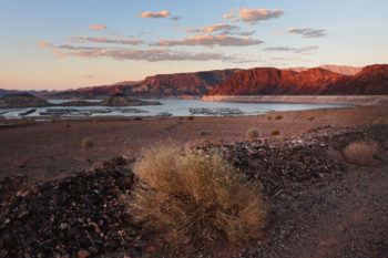 the sun setting behind lake mead, surrounded by dry landscape
