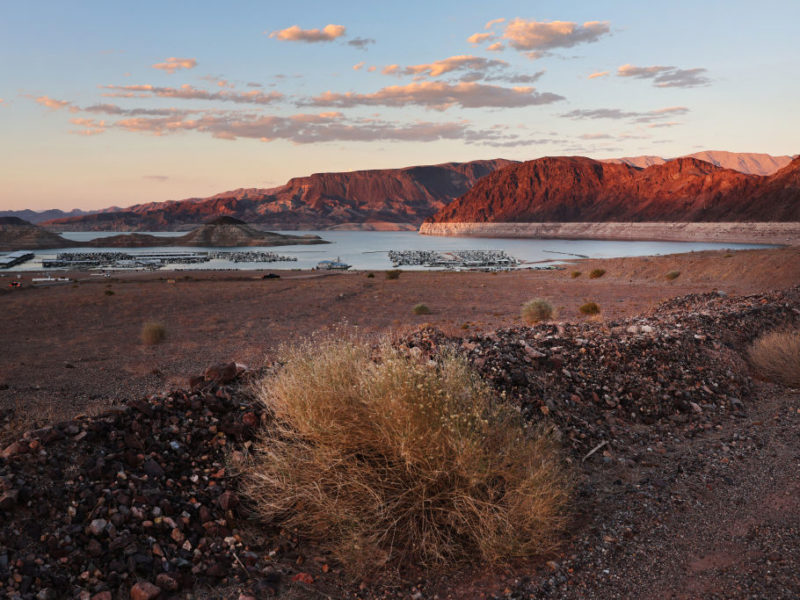 the sun setting behind lake mead, surrounded by dry landscape