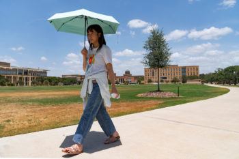 a woman holding a blue umbrella walks through campus