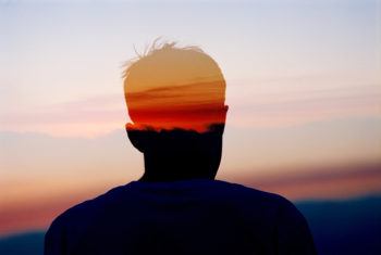 Concept photo of a man's head in silhouette layered against the sky at sunset