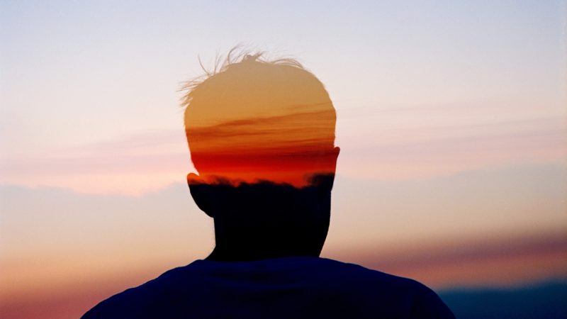 Concept photo of a man's head in silhouette layered against the sky at sunset