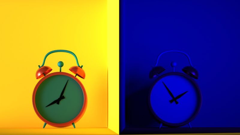 Two alarm clocks side-by-side against yellow and blue backgrounds representing day and night.