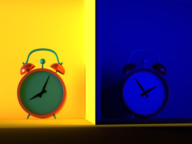 Two alarm clocks side-by-side against yellow and blue backgrounds representing day and night.