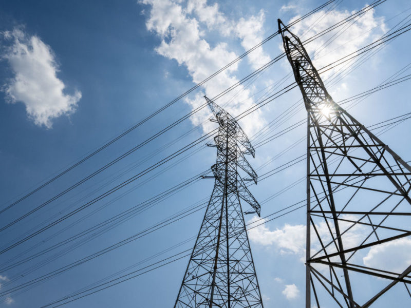 view from below of electric transmission towers against a blue sky on a sunny day