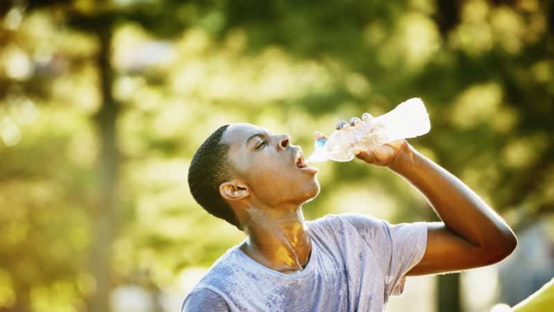 Young man drinking out of a water bottle on a sunny day