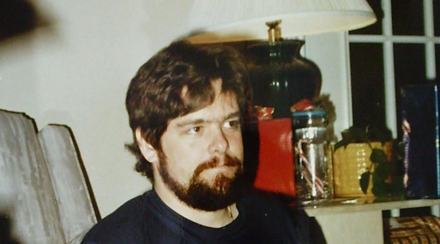 an old photo of a man with brown hair and beard sitting down in a living room
