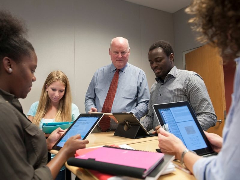 2 older gentlemen using electronic tablets circled with 3 female students who are also using electronic tablets