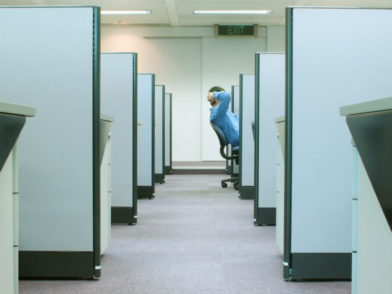 A man reclining in his chair positioned in a row of cubicles in an office