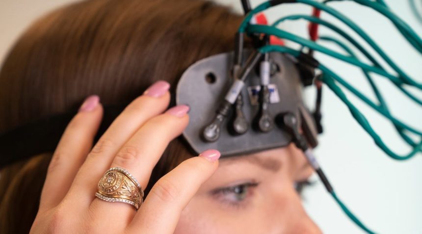 a photo of a woman with an Aggie Ring and a series of cables attached to a device on the front of her head