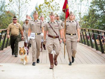 Cadets and Reveille marching over a bridge