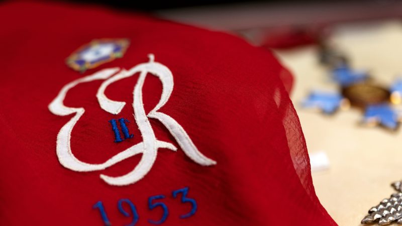 a close up photo of a red scarf with the letters ER embroidered in white, along with a roman numeral 2 and the year 1953 in blue