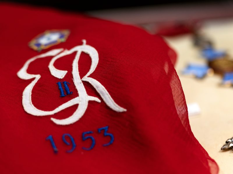 a close up photo of a red scarf with the letters ER embroidered in white, along with a roman numeral 2 and the year 1953 in blue