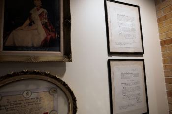 a photo of two framed documents on a white wall - the signatures of Prince Philip and Queen Elizabeth II appear at the bottom and top of the documents, respectively