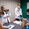 a photo of several young people in scrubs, lab coats and medical masks gathered around a table holding two small dogs
