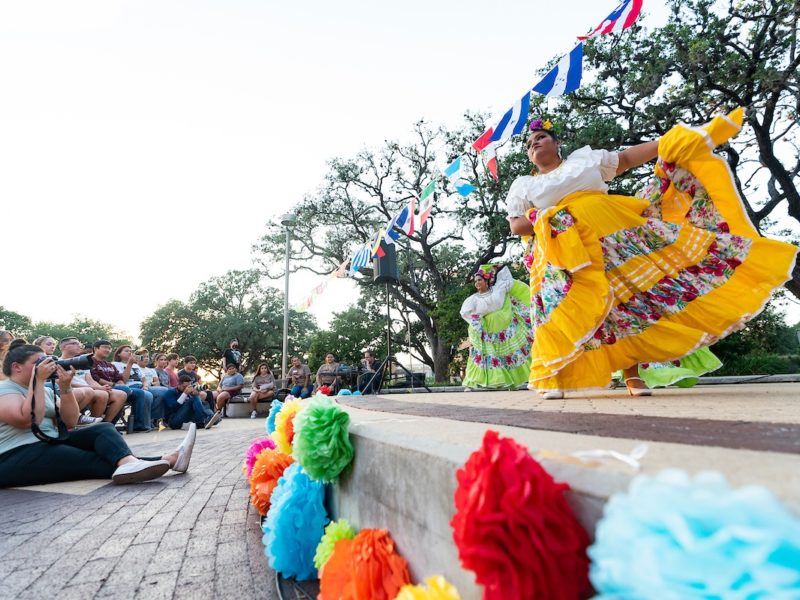 wide angle view of ballet folklorico dancers in colorful dresses performing in front of students in rudder plaza