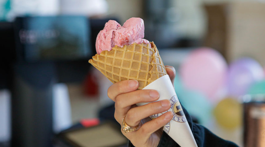 close-up photo of a hand holding a waffle cone with strawberry ice cream