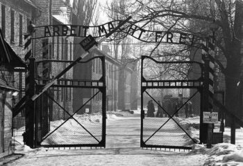 Black and white archival photo of the gates of the concentration camp at Auschwitz
