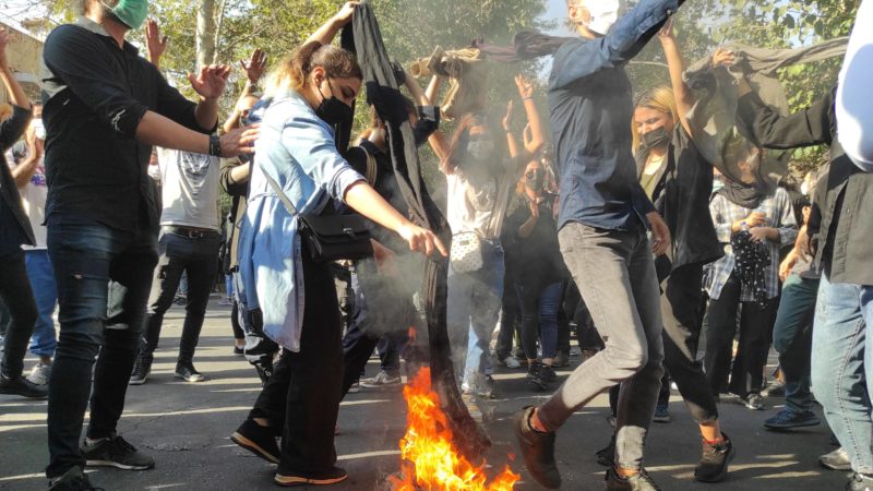 People protesting in Iran stand around a burning hijab in the street