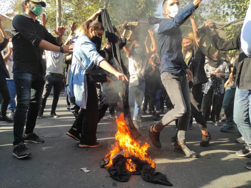 People protesting in Iran stand around a burning hijab in the street