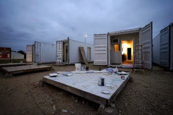 a photo of a row of white shipping containers. the interior of one container can be seen, containing lights, doors and cabinets.