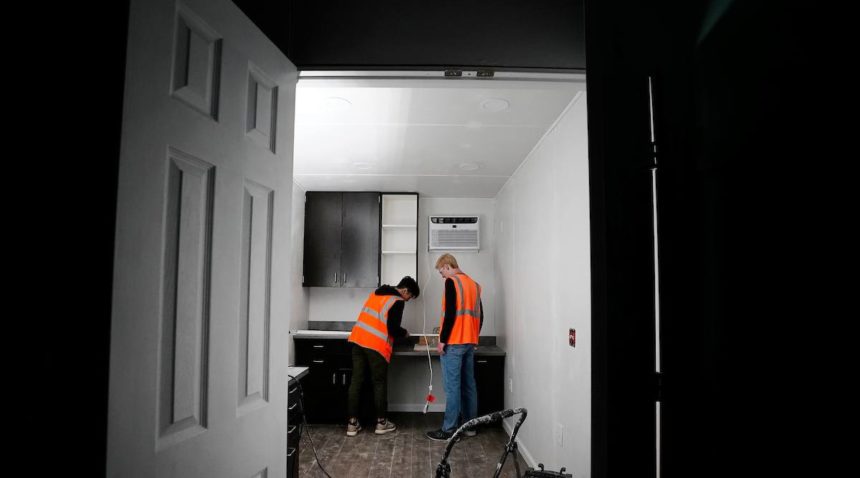 a photo of two young men in orange safety vests working inside a shipping container clinic