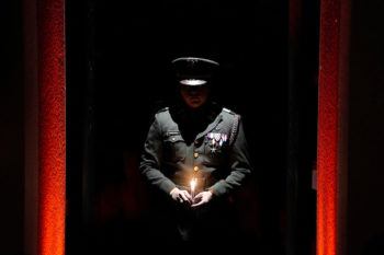 A cadet standing in darkness, lit only by the light from the candle he holds in his hands.