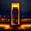 A photo of the bonfire memorial illuminated at night with a cadet standing in a portal. In the background, other cadets are standing at attention.