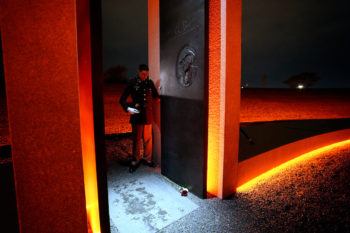 A cadet stands inside a portal holding a candle. The likeness of a fallen Aggie is visible engraved inside the portal.