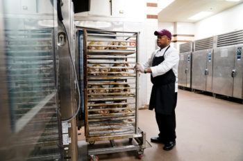 Chef Luke Rayford Standing in a kitchen next to vertical racks of uncooked turkeys
