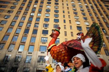 a giant inflatable turkey float in a parade with a large apartment building in the background